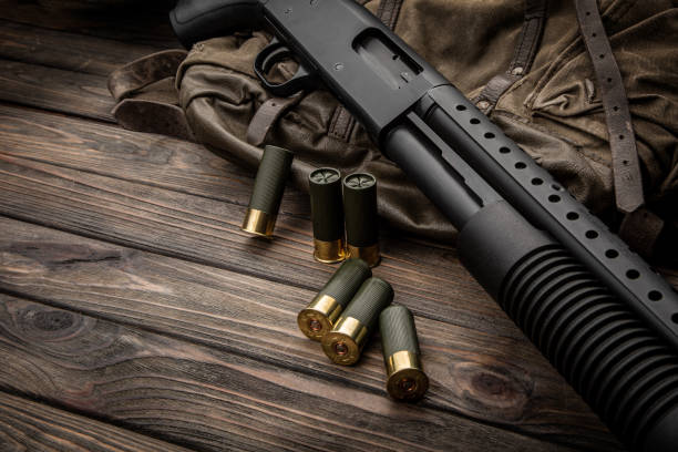 A black 12-gauge pump-action shotgun and ammo are on a canvas backpack. A smooth-bore weapon with a plastic stock. Dark background.