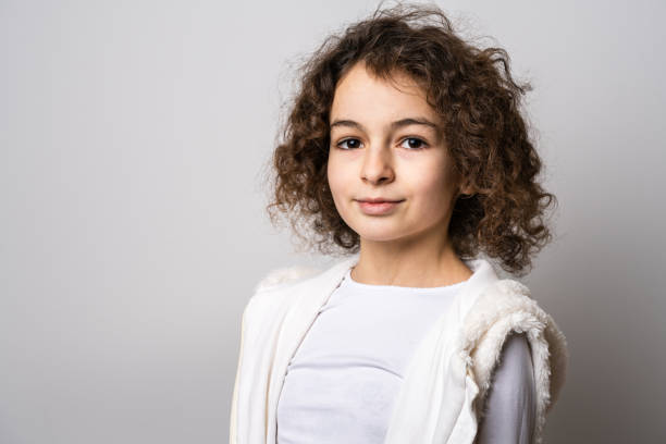 one small caucasian girl ten years old with curly hair front view portrait close up standing in front of white background looking to the camera copy space - 10 11 years child human face female imagens e fotografias de stock
