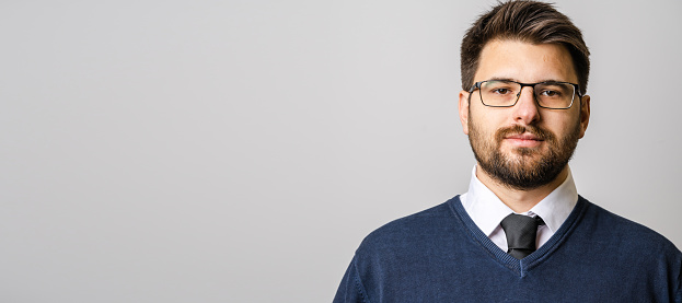 Portrait of one adult caucasian man 30 years old with beard and eyeglasses looking to the camera in front of white wall background wearing sweater young businessman success concept copy space