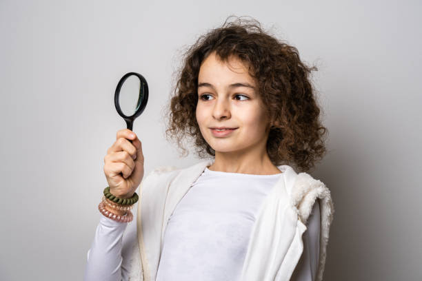 one small caucasian girl ten years old with curly hair front view portrait close up standing in front of white background looking to the camera holding magnifying lens education and learning concept - magnifying glass lens holding europe imagens e fotografias de stock