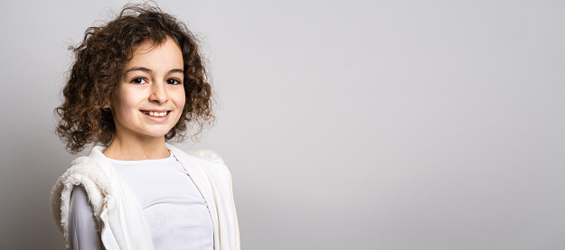 One small caucasian girl ten years old with curly hair front view portrait close up standing in front of white background looking to the camera smiling happy and joy copy space