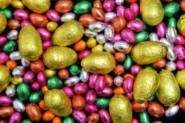 istock Small pink, orange, green and silver foil wrapped chocolate easter eggs with larger yellow eggs, against a pale wood background. 1388622994