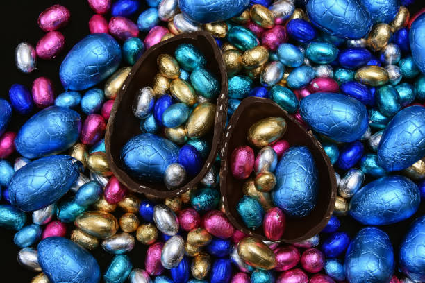 istock Pile of multi colored and different sizes of colourful foil wrapped chocolate easter eggs in blue, pink, silver, and gold with two halves of a large brown milk chocolate egg in the middle and mini eggs inside. 1388623009