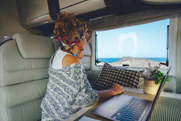 People in work and travel online modern activity business lifestyle. Woman looking outside from camper van interior sitting at the table with laptop computer. Concept of digital nomad life stock photo