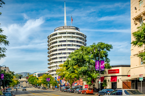 Cars and pedestrians move beside the Capitol Records Building in Hollywood, Los Angeles, California, USA on a sunny day.