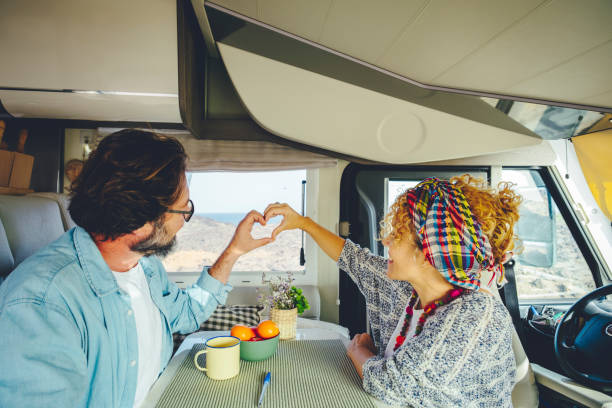 Happy mature couple doing heart gesture sign with hands together inside modern camper van vehicle. Concept of traveler and road trip holiday vacation lifestyle. Man and woman stock photo