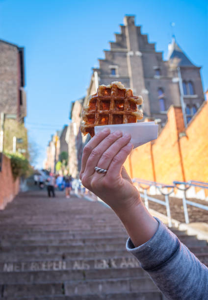 Delicious belgian waffle held in front of blurred background of Montagne de Bueren staircase in Liege, which is the city's top tourist attraction Tasty belgian waffle displayed in front of the famous tourist attraction liege belgium stock pictures, royalty-free photos & images