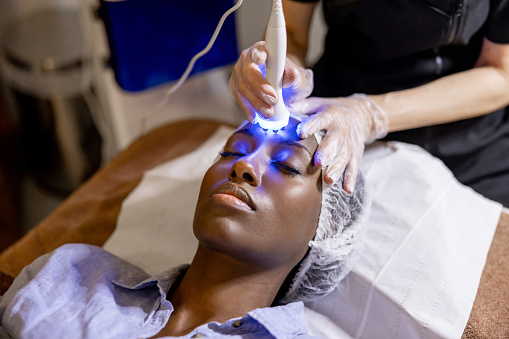 African American woman at the spa getting a beauty treatment on her face using ultrasound and light therapy