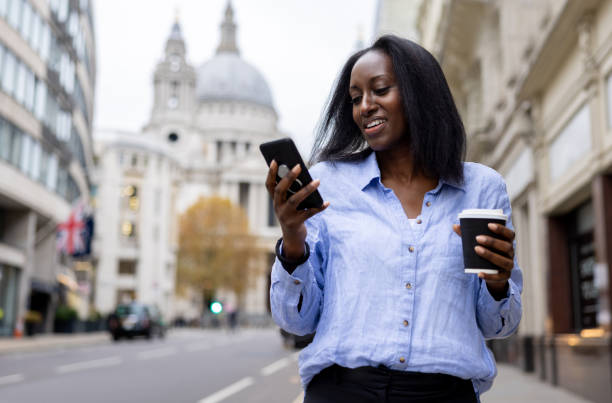 Business woman drinking coffee on the street while checking her cell phone