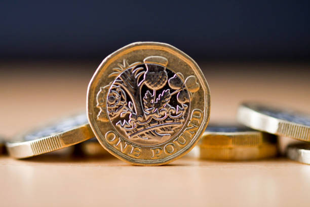 Close up view of British one pound coins British one pound coin standing on its edge with other coins in the baclground. No people. one pound coin stock pictures, royalty-free photos & images