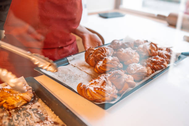 fresh homemade cinnamon rolls or cinnamon buns are on a baking sheet board, there is an unrecognizable person wearing an apron in the background - cinnamon buns people bildbanksfoton och bilder