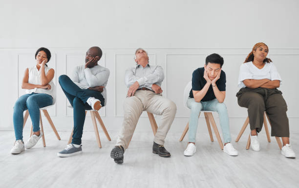 toma de un grupo diverso de personas que parecen aburridas mientras están sentadas en la fila sobre un fondo blanco - waiting fotografías e imágenes de stock