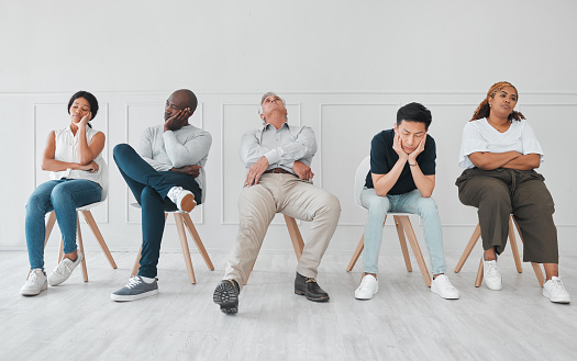 Shot of a diverse group of people looking bored while sitting in line against a white background