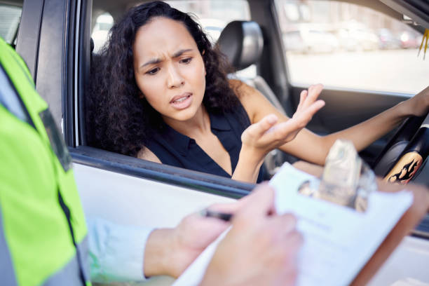 Shot of a young businesswoman looking upset at receiving a ticket from a traffic officer stock photo