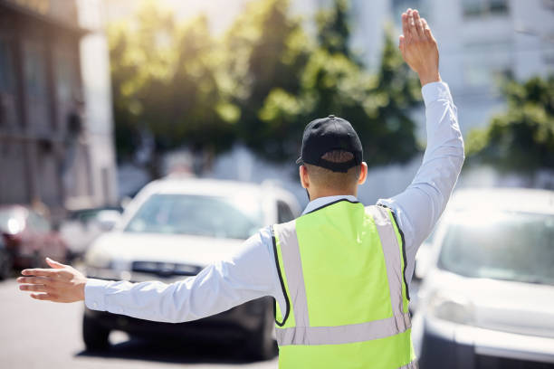 Rearview shot of a traffic warden guiding vehicles outdoors Directing and controlling the flow of traffic graffic stock pictures, royalty-free photos & images