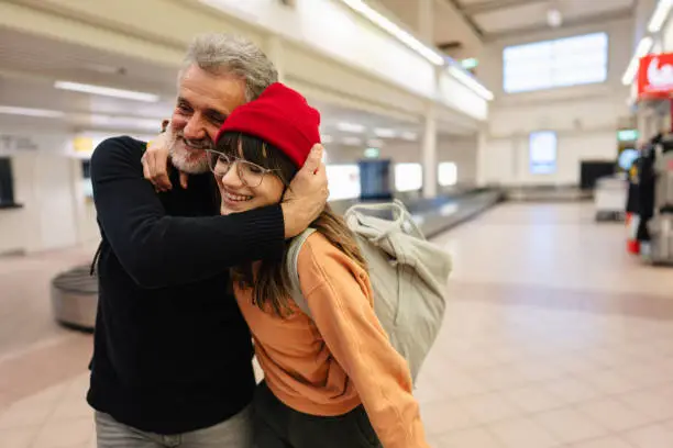 Photo of a young woman and her senior father meeting at the airport after a long time, reuniting after pandemic separations and isolation.