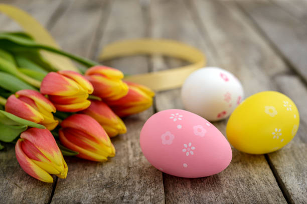 A group of colorful decorated Easter eggs and a bouquet of tulips on a rustic wooden table. Easter concept.