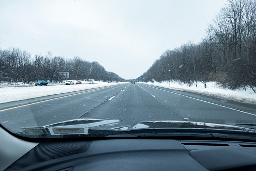 Car driver point of view looking through windshield while speeding along a winter snow flurry expressway highway near Rochester, in western New York State.