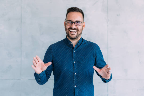 Businessman talking during video call in the office. Handsome elegant male entrepreneur discussing while having a conference call in the office. Portrait of confident young male employee looking at camera  talking on video call in the office. presenter stock pictures, royalty-free photos & images