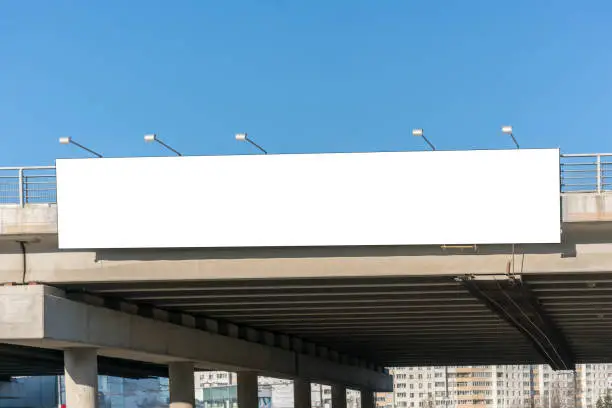 Photo of Long white empty signboard hanging on concrete urban bridge