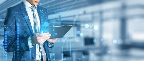 istock Close up of businessman hand using tablet in blurry bokeh office interior with creative glowing business chart and wide mock up place for your advertisement. Growth, sales and market concept. Double exposure. 1388644266
