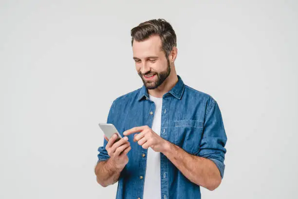 Photo of Happy caucasian young man using smart phone cellphone for calls, social media, mobile application online isolated in white background
