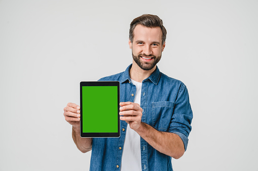 Happy caucasian young man student freelancer holding showing digital tablet with green mockup screen for ad copyspace isolated in white background