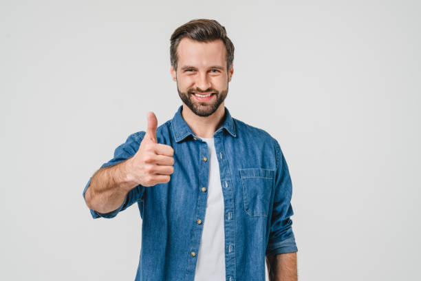 closeup portrait of positive caucasian young man in denim casual clothes showing thumb up for good quality checkup, smiling with toothy smile isolated in white background - thumbs up business people isolated imagens e fotografias de stock
