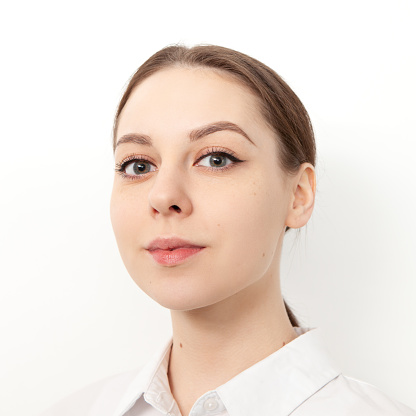 Close-up studio portrait of an attractive 20 year old woman with brown hair in a white shirt on a white background