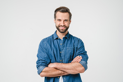 Confident caucasian young man in casual denim clothes with arms crossed looking at camera with toothy smile isolated in white background