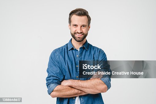 istock Confident caucasian young man in casual denim clothes with arms crossed looking at camera with toothy smile isolated in white background 1388648617