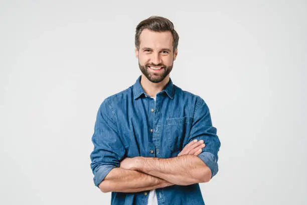 Photo of Confident caucasian young man in casual denim clothes with arms crossed looking at camera with toothy smile isolated in white background