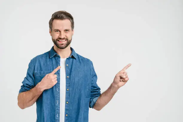 Happy smiling caucasian man freelancer student in denim clothes pointing showing at copy space freespace for ad isolated in white background
