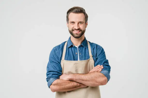 Photo of Confident smiling caucasian young man student bartender barista in apron with arms crossed looking at camera isolated in white background. Takeaway food