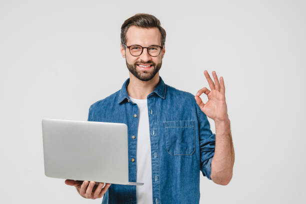 istock Happy successful caucasian young man freelancer student showing okay gesture, using laptop for remote studies, e-learning, working on distance isolated in white background 1388649914