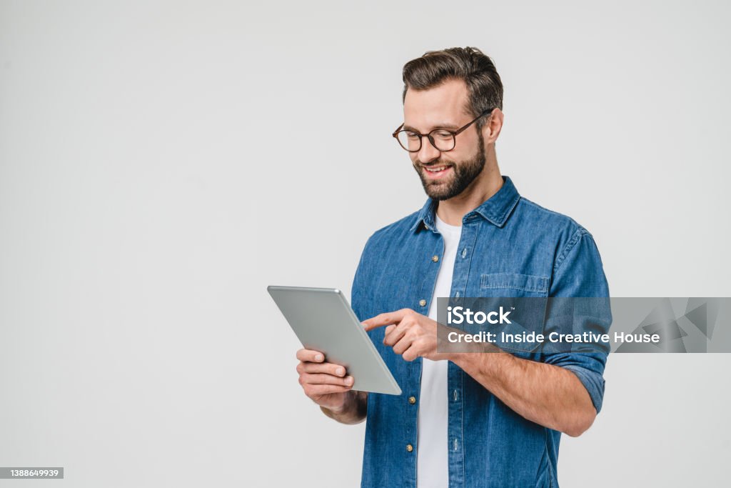 Cheerful caucasian young man student freelancer using digital tablet for social media, e-banking, mobile application, e-learning isolated in white background - Royalty-free Homens Foto de stock Cheerful caucasian young man student freelancer using digital tablet for social media, e-banking, mobile application, e-learning isolated in white background - Royalty-free Homens Foto de stock
