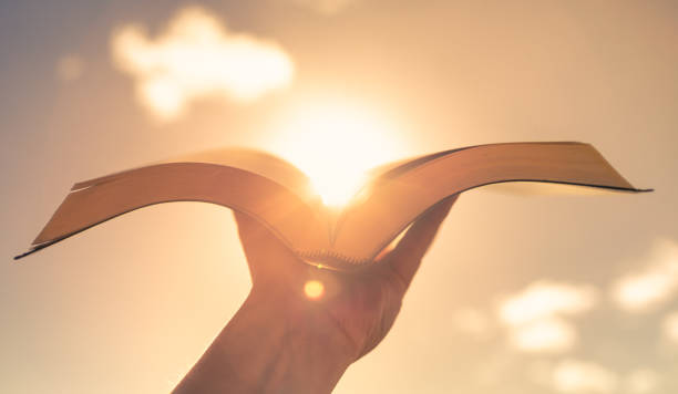 hombre sosteniendo la biblia contra un cielo al atardecer - biblia fotografías e imágenes de stock