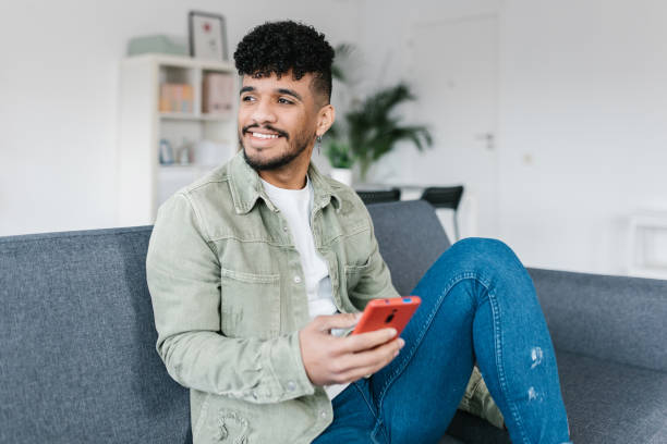 istock Young african american man using mobile phone relaxing on sofa at home 1388654506