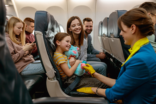 Smiling little girl holding toy and looking at flight attendant while sitting next to parents in passenger plane