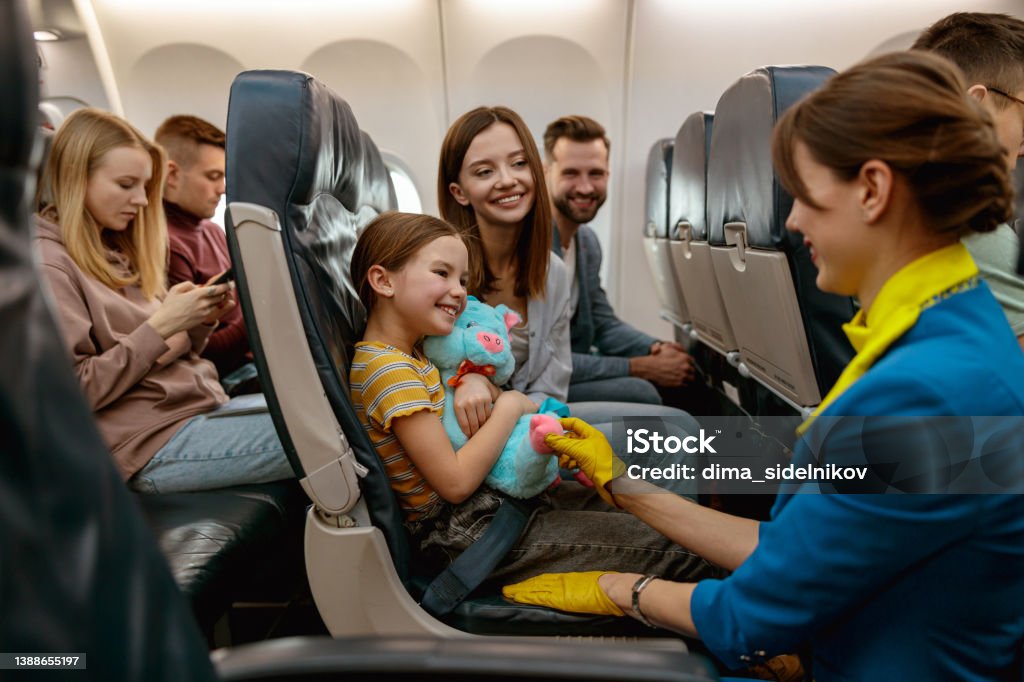 Family with child talking with stewardess in airplane Smiling little girl holding toy and looking at flight attendant while sitting next to parents in passenger plane Airplane Stock Photo