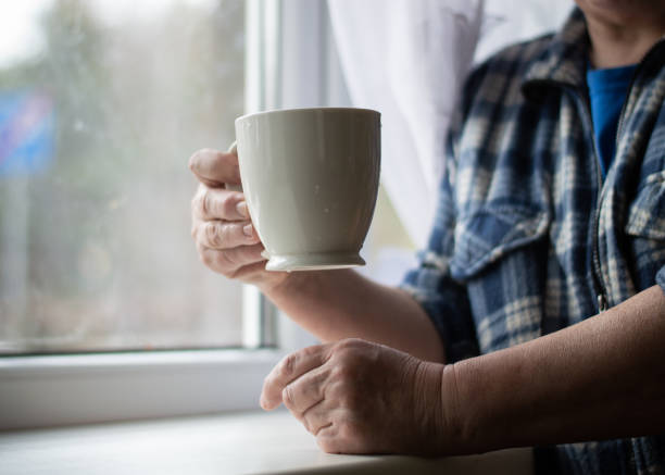 istock Senior holding a cup of coffee while standing at the window 1388659587