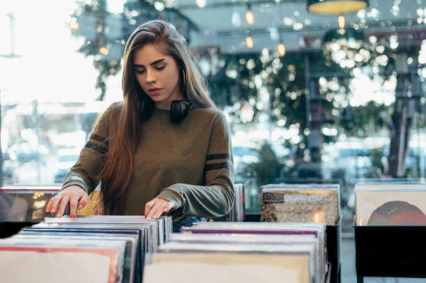 Woman choosing vinyl record in music record shop Gorgeous young woman looking for vinyl records in a vintage store. Vintage and retro style. record analog audio stock pictures, royalty-free photos & images