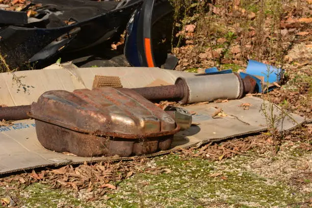 Catalytic converter and exhaust system laying on cardboard outdoors. The worn and rusted system was discarded outdoors.