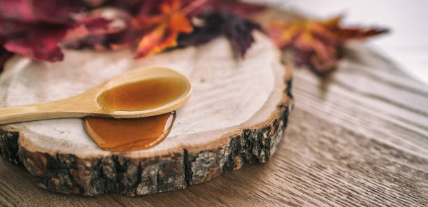 sirop d’érable cabane à sucre un restaurant de sucre de la ferme québécoise érable sève célèbre liquide sucré dégoulinant d’une cuillère en bois sur bûche de bois. bannière rustique de cabane à sucre panoramique avec des feuilles rouges - maple syrup sugar shack photos et images de collection