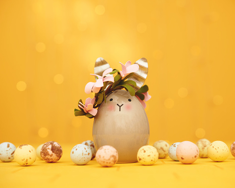Easter background with Easter bunny wearing a flower crown and small chocolate Easter eggs in a yellow setting