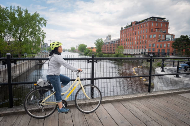 Mature Asian Woman Cycling Across Bridge Over Canal stock photo