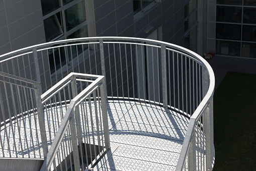 modern spiral staircase with protective railing and handrail outside of a modern structure, part of a very neat school or company organization, with vegetation in the gardens and large windows, of humanistic but functional concept, illuminated in full sunlight
