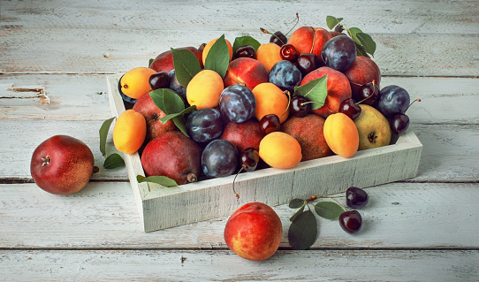 Fresh colorful berries and fruits in a box on a wooden table, harvesting
