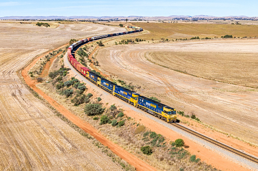 Crystal Brook, Australia - March 11, 2022: Aerial view, Pacific National Sydney to Perth intermodal container train with 4 powerful GE NR-class diesel locomotives, winding around S-curves surrounded by agricultural farmland in rural South Australia.