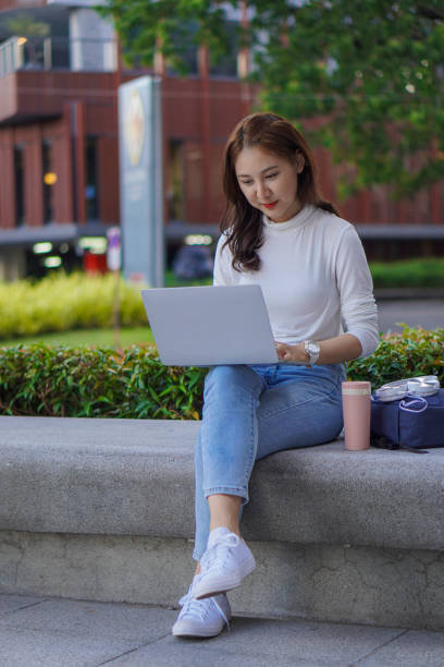 istock Cute young Asian female student working on a laptop computer outdoors, studying concepts, working in the public domain. 1388708826
